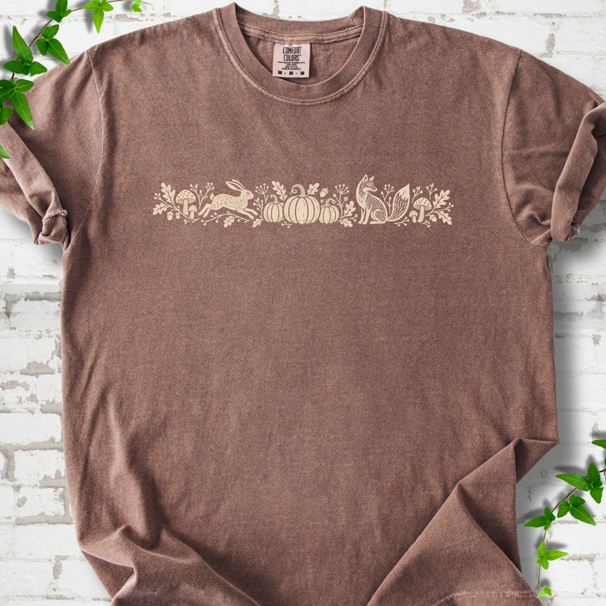 Espresso Comfort Colors® T-shirt with a folk-style Woodland Harvest design of mushrooms, pumpkins and woodland animals.
