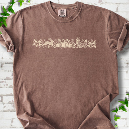 Espresso Comfort Colors® T-shirt with a folk-style Woodland Harvest design of mushrooms, pumpkins and woodland animals.