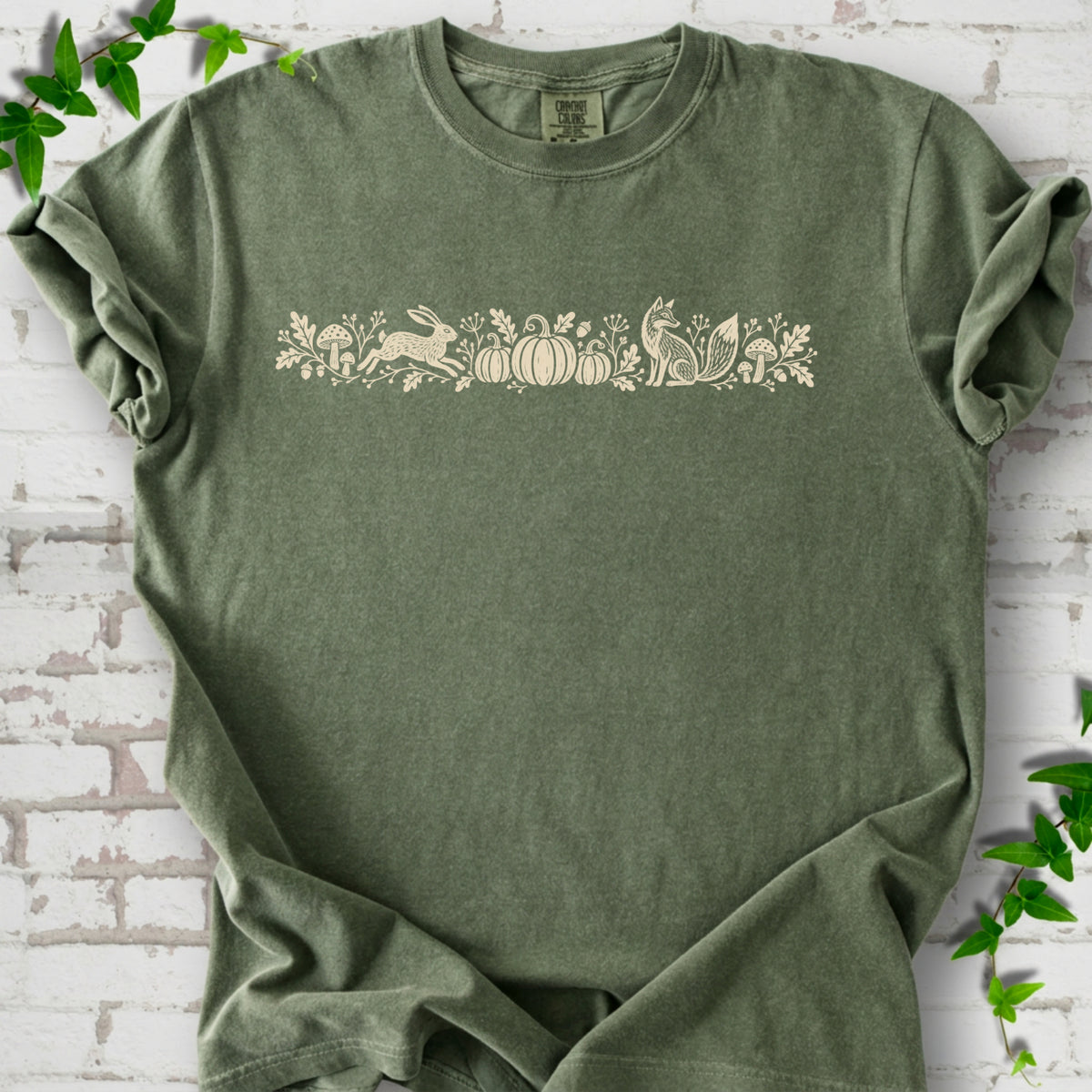Moss Comfort Colors® T-shirt with a folk-style Woodland Harvest design of mushrooms, pumpkins and woodland animals.