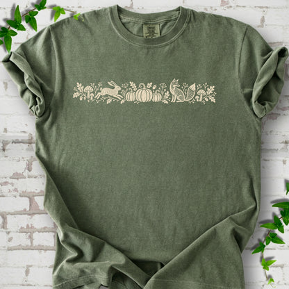 Moss Comfort Colors® T-shirt with a folk-style Woodland Harvest design of mushrooms, pumpkins and woodland animals.