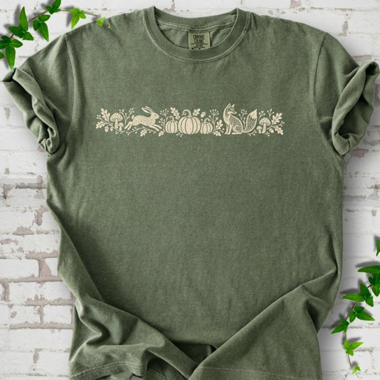 Moss Comfort Colors® T-shirt with a folk-style Woodland Harvest design of mushrooms, pumpkins and woodland animals.