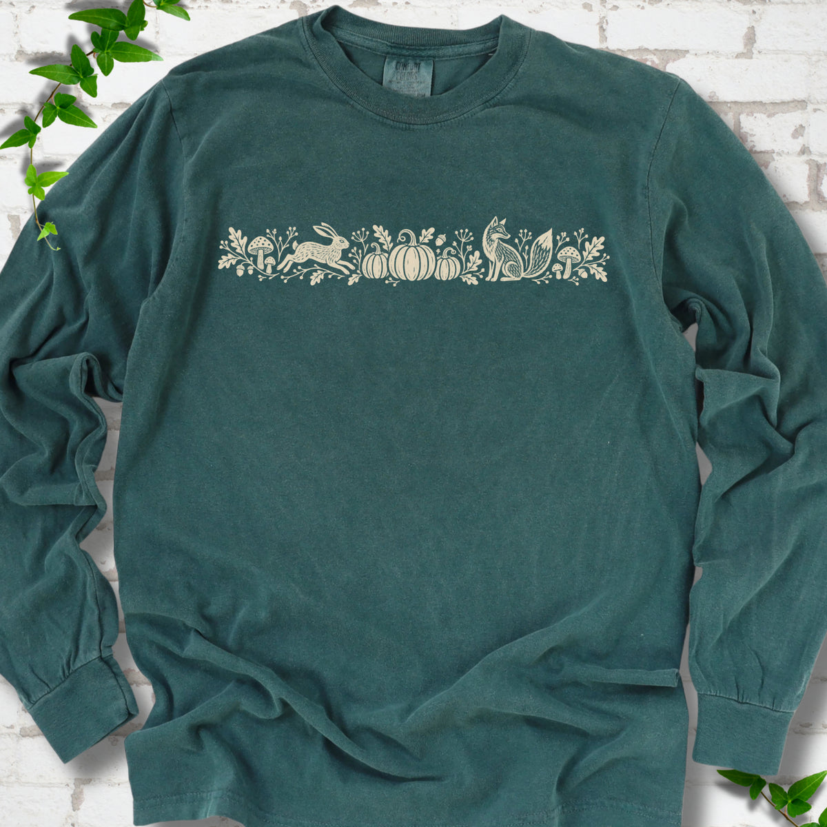 Blue Spruce Comfort Colors® long sleeve shirt with a folk-style Woodland Harvest design of mushrooms, pumpkins and woodland animals.