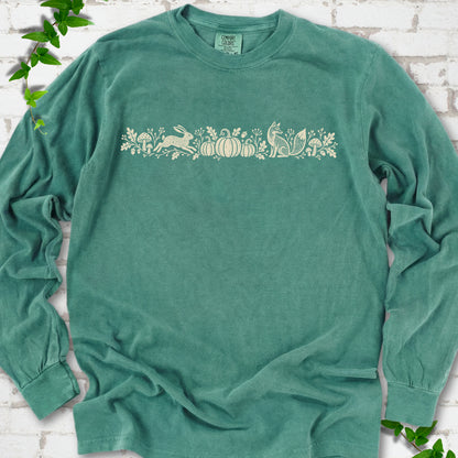 Light Green Comfort Colors® long sleeve shirt with a folk-style Woodland Harvest design of mushrooms, pumpkins and woodland animals.