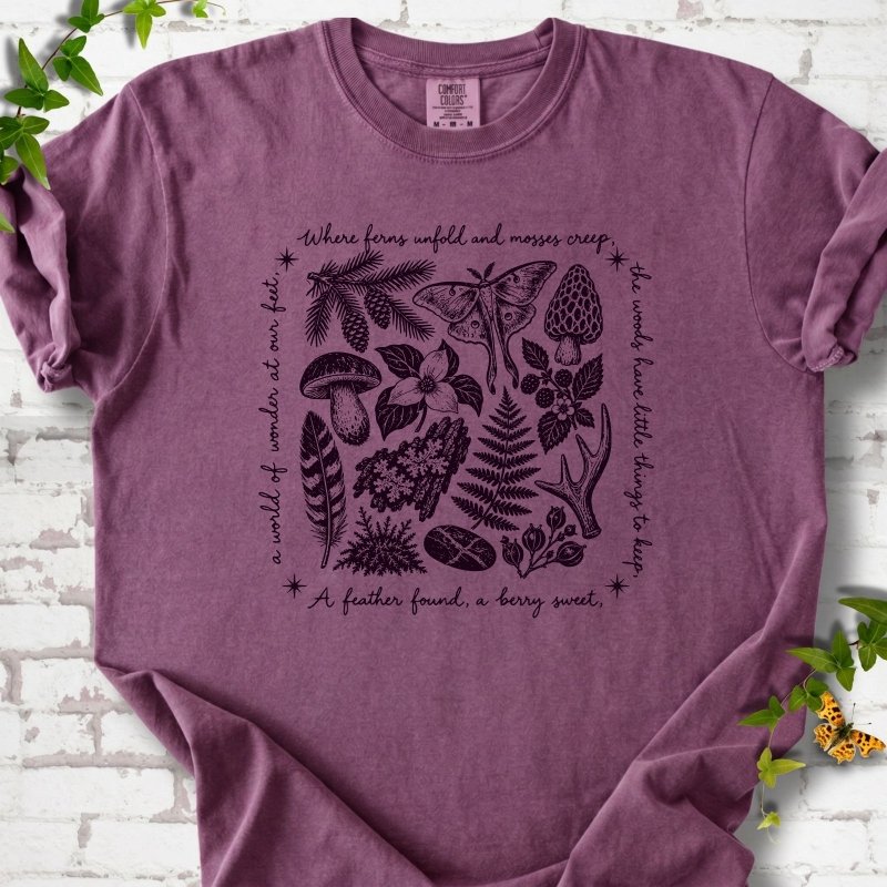 Berry purple short-sleeve tee with woodland finds engraving in dark plum ink, framed by "a world of wonder at our feet".