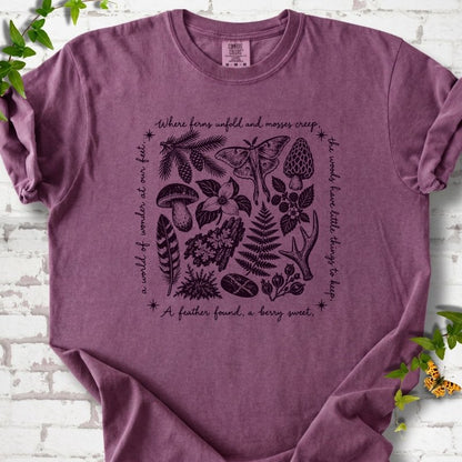 Berry purple short-sleeve tee with woodland finds engraving in dark plum ink, framed by "a world of wonder at our feet".