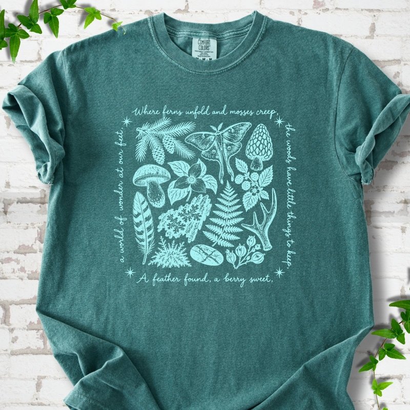 Seafoam green short-sleeve tee with woodland finds engraving in light ink, framed by "a world of wonder at our feet".