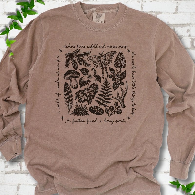 Espresso brown long-sleeve tee with woodland finds engraving in dark brown ink, framed by "a world of wonder at our feet".