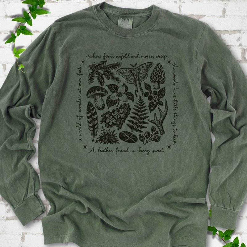 Hemp green long-sleeve tee with woodland finds engraving in dark green ink, framed by "a world of wonder at our feet".