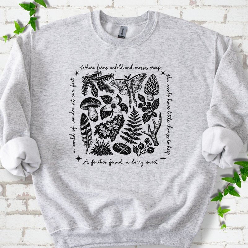 Ash gray crewneck sweatshirt with woodland finds engraving in black ink, framed by "a world of wonder at our feet".