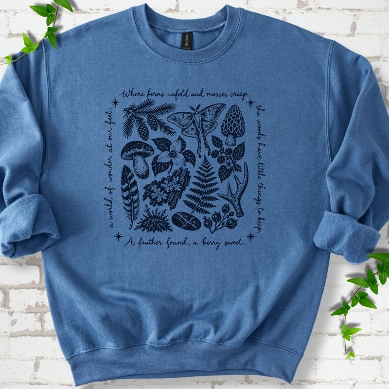 Indigo blue crewneck sweatshirt with woodland finds engraving in navy ink, framed by "a world of wonder at our feet".