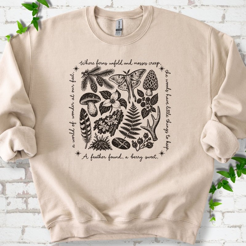 Sand crewneck sweatshirt with woodland finds engraving in dark ink, framed by "a world of wonder at our feet".