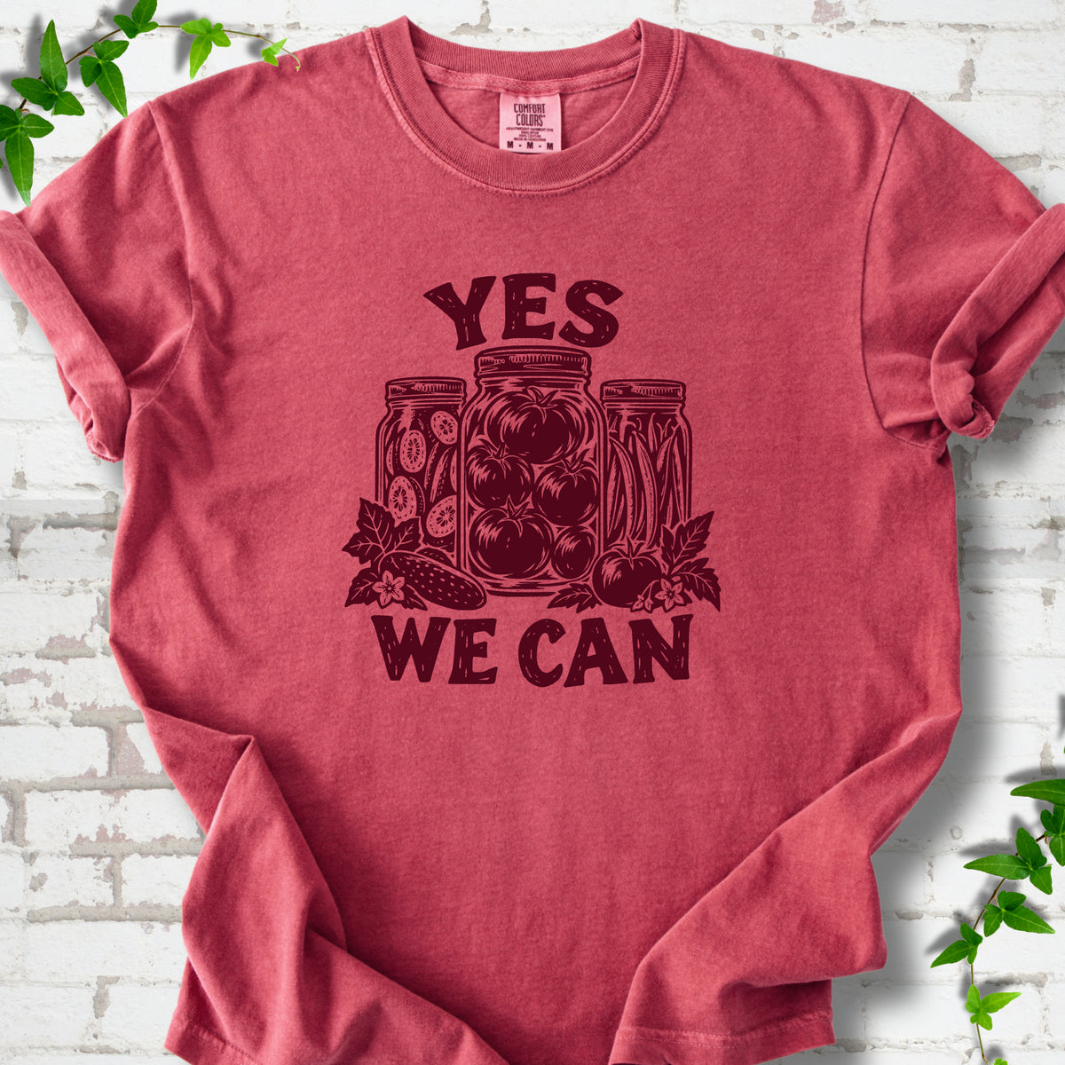 Crimson Comfort Colors® T-shirt flat lay featuring preserved tomatoes in jars and the words “Yes We Can.”