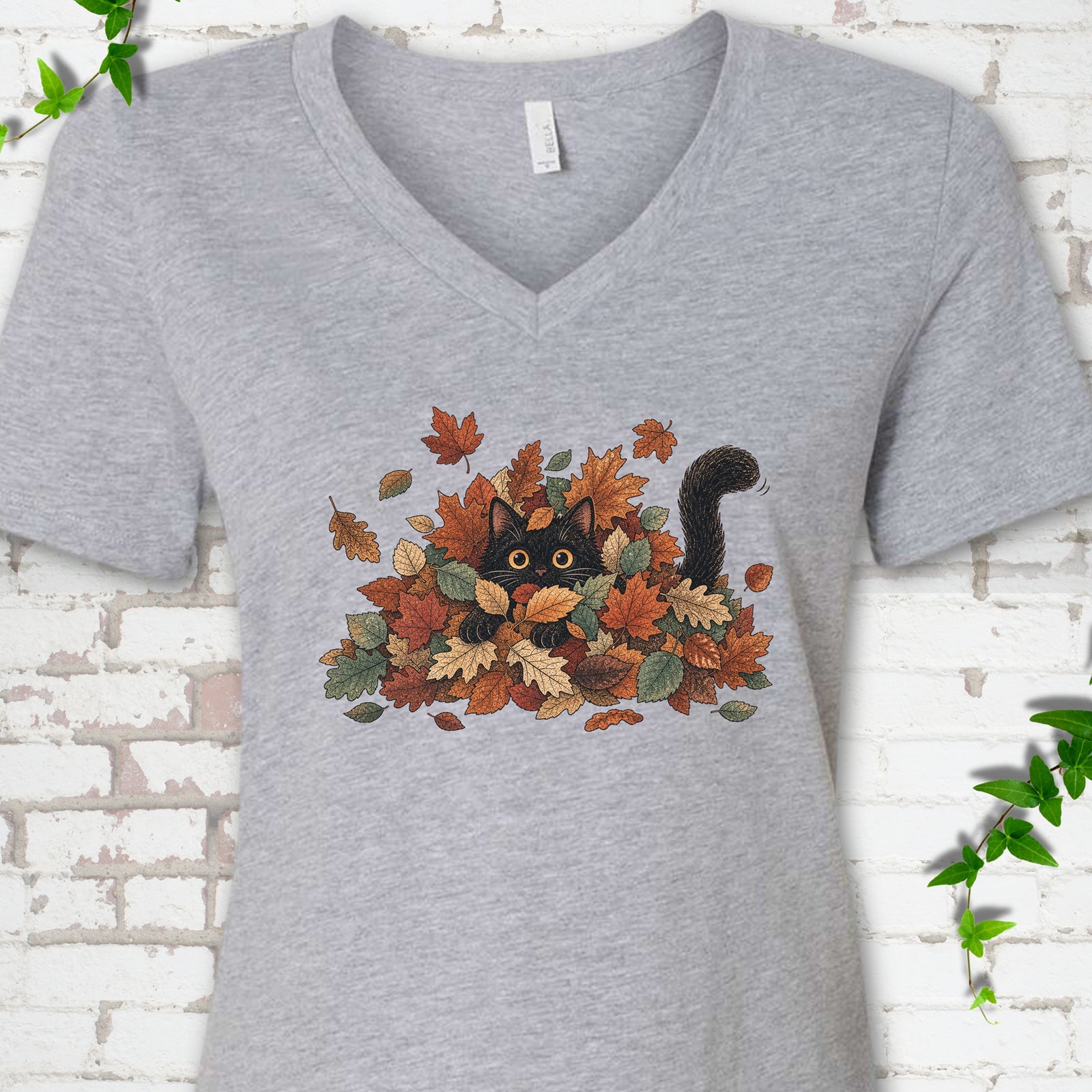 Athletic Heather Bella Canvas® V-neck T-shirt flat lay featuring a black cat peeking from a pile of orange and green autumn leaves.
