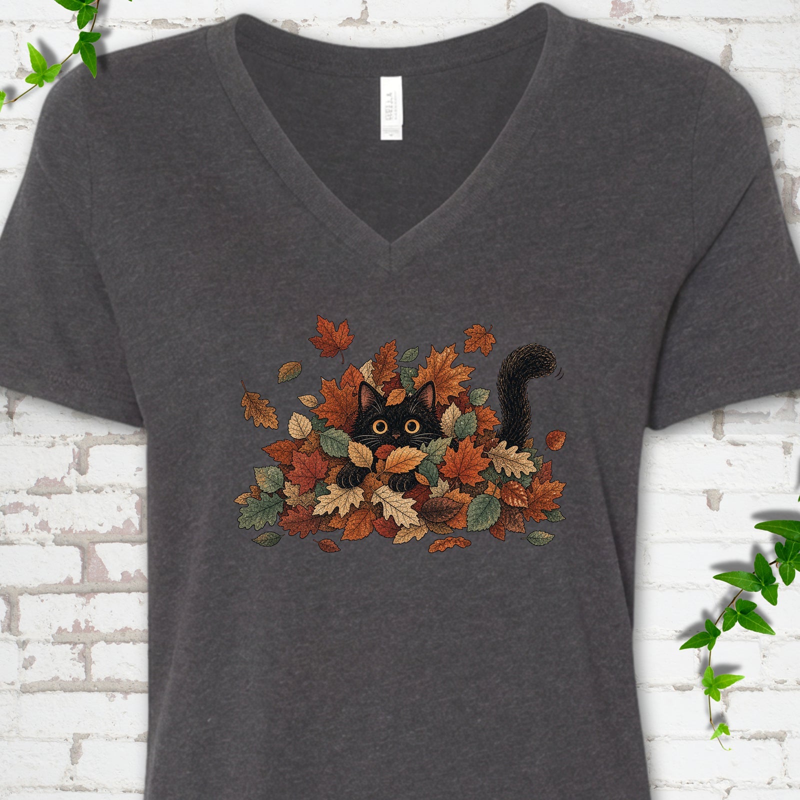 Dark Grey Heather Bella Canvas® V-neck T-shirt flat lay featuring a black cat peeking from a pile of orange and green autumn leaves.