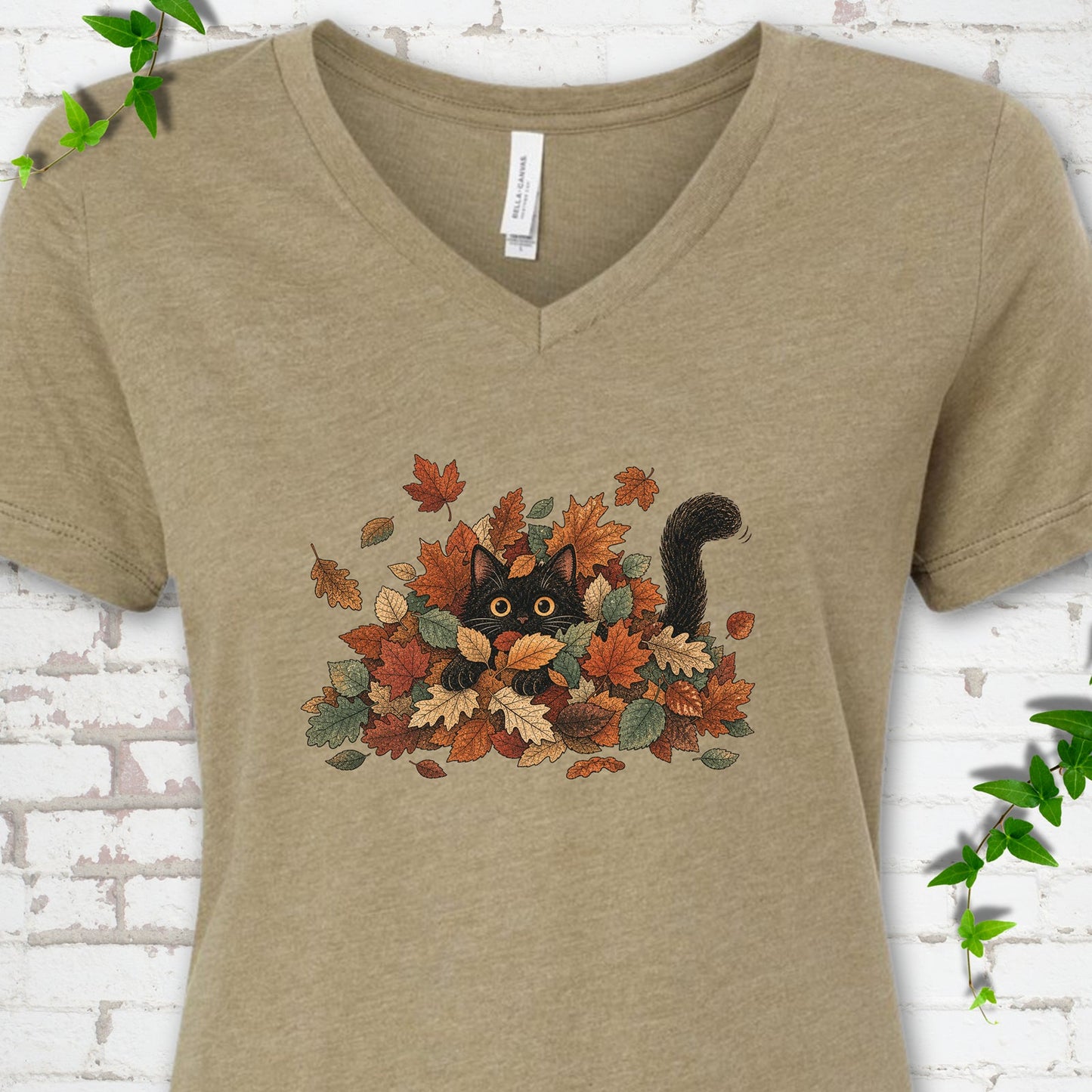 Heather Olive Bella Canvas® V-neck T-shirt flat lay featuring a black cat peeking from a pile of orange and green autumn leaves.