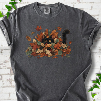 Pepper Comfort Colors® T-shirt flat lay featuring a black cat peeking from a pile of orange and green autumn leaves.