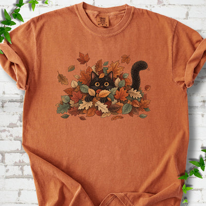 Yam Comfort Colors® T-shirt flat lay featuring a black cat peeking from a pile of orange and green autumn leaves.