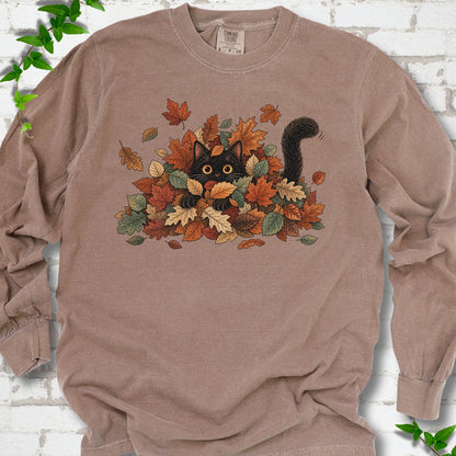 Espresso Comfort Colors® long sleeve T-shirt flat lay featuring a black cat peeking from a pile of orange and green autumn leaves.