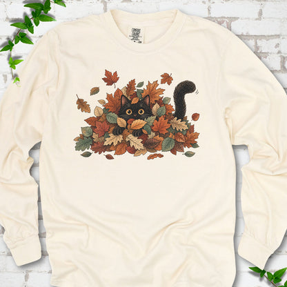 Ivory Comfort Colors® long sleeve T-shirt flat lay featuring a black cat peeking from a pile of orange and green autumn leaves.
