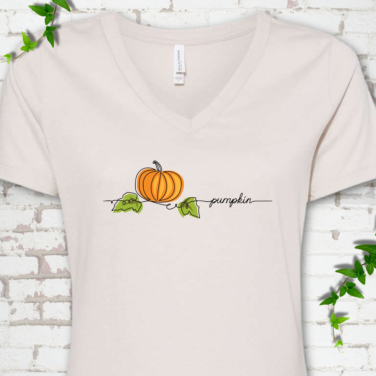 Heather Dust Bella Canvas® V-neck T-shirt flat lay featuring a minimalist orange pumpkin, green leaves and delicate black script.