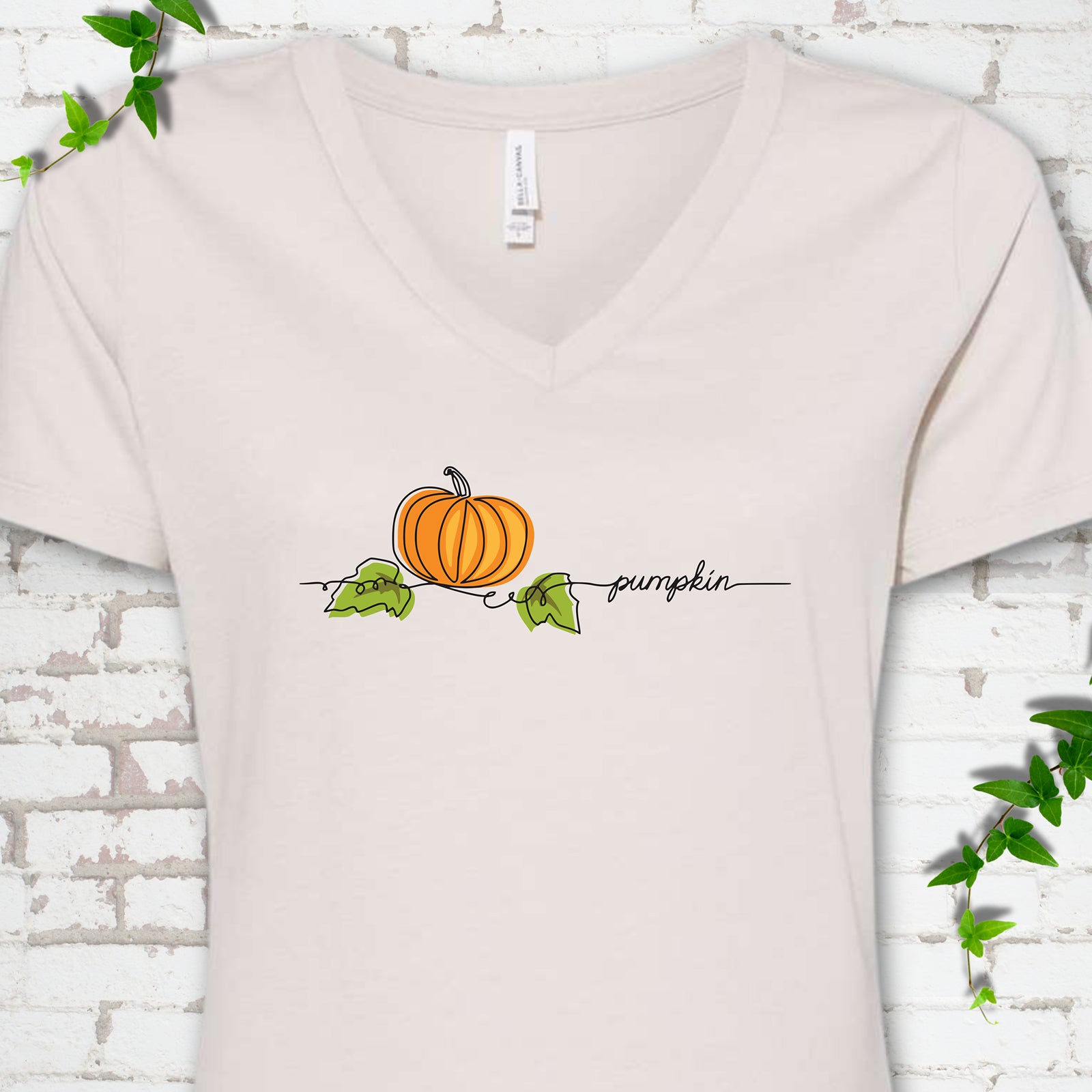 Heather Dust Bella Canvas® V-neck T-shirt flat lay featuring a minimalist orange pumpkin, green leaves and delicate black script.