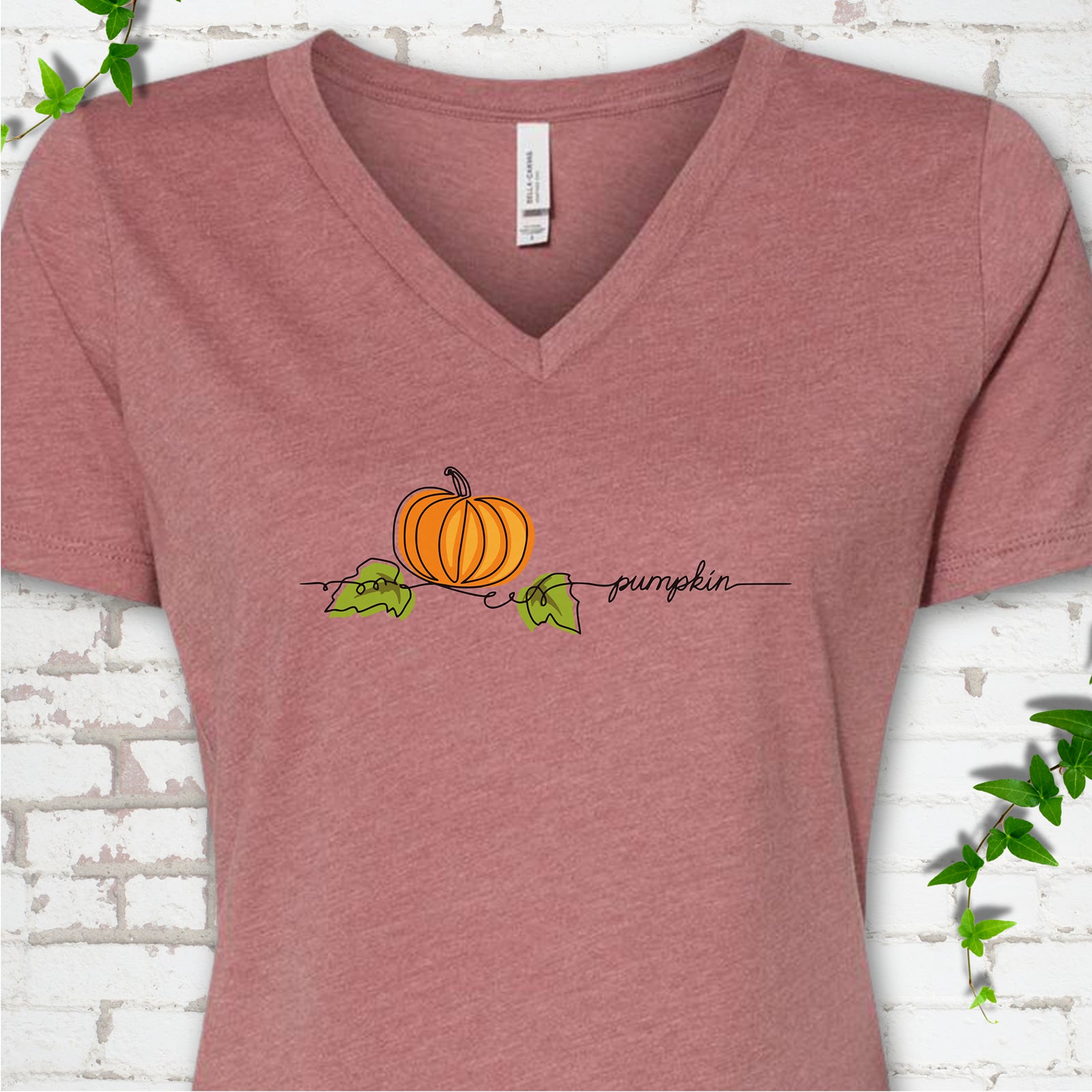 Heather Mauve Bella Canvas® V-neck T-shirt flat lay featuring a minimalist orange pumpkin, green leaves and delicate black script.
