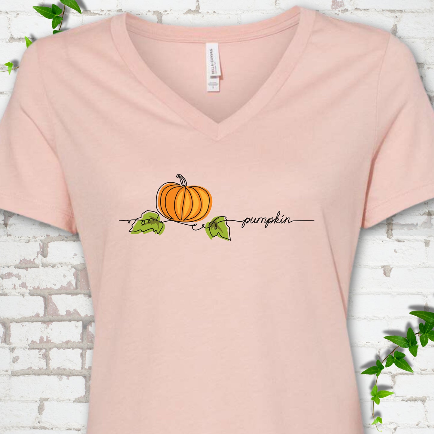 Heather Peach Bella Canvas® V-neck T-shirt flat lay featuring a minimalist orange pumpkin, green leaves and delicate black script.