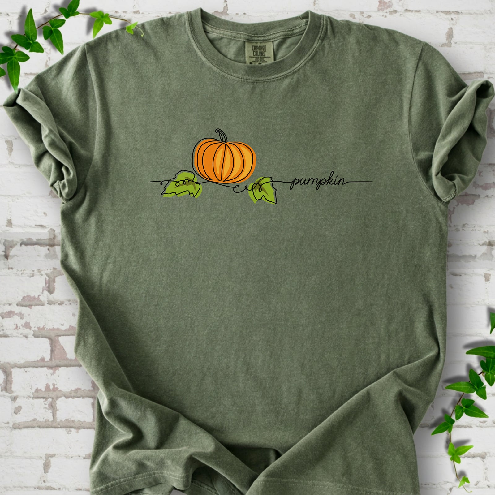 Moss Comfort Colors® T-shirt flat lay featuring a minimalist orange pumpkin, green leaves and delicate black script.