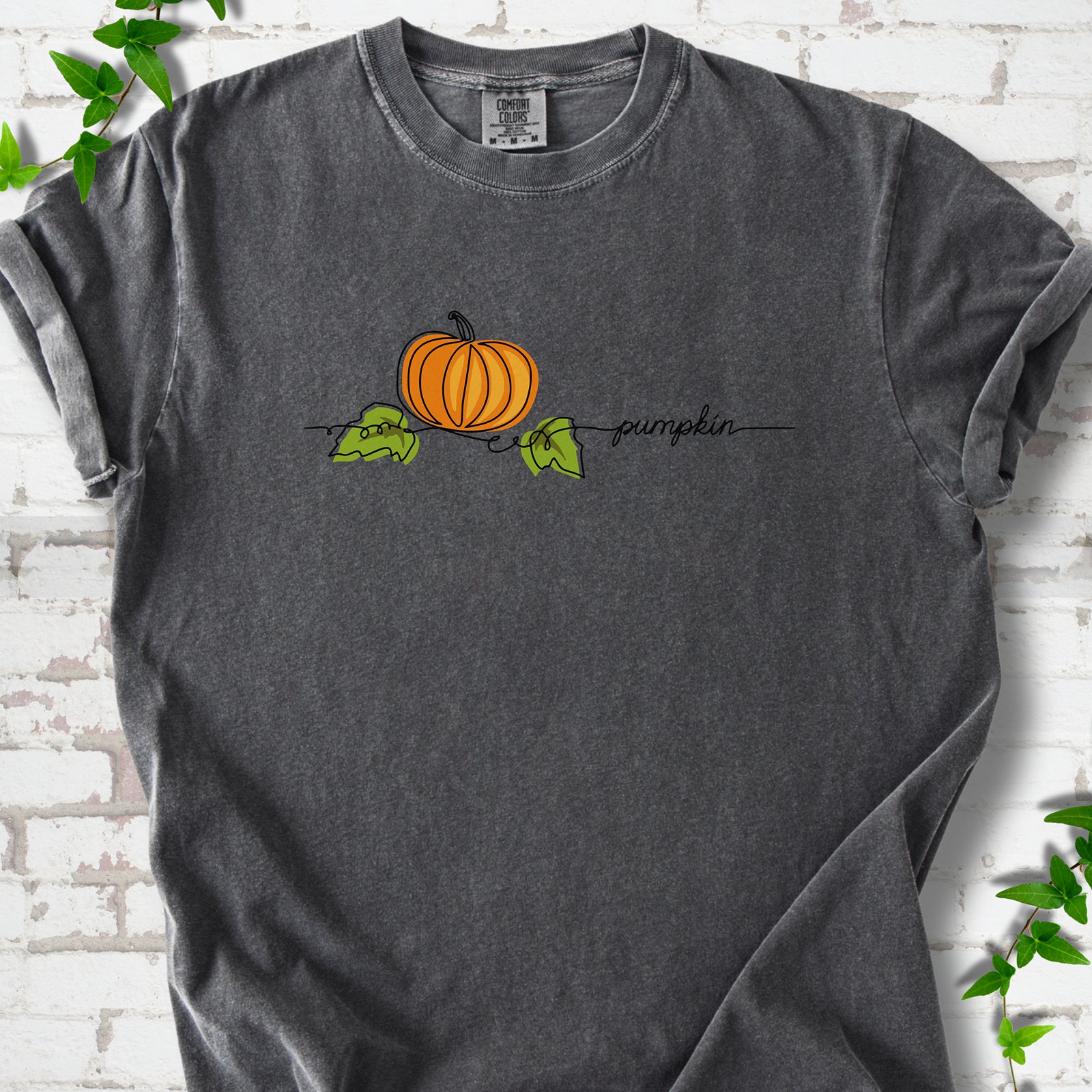 Pepper Comfort Colors® T-shirt flat lay featuring a minimalist orange pumpkin, green leaves and delicate black script.