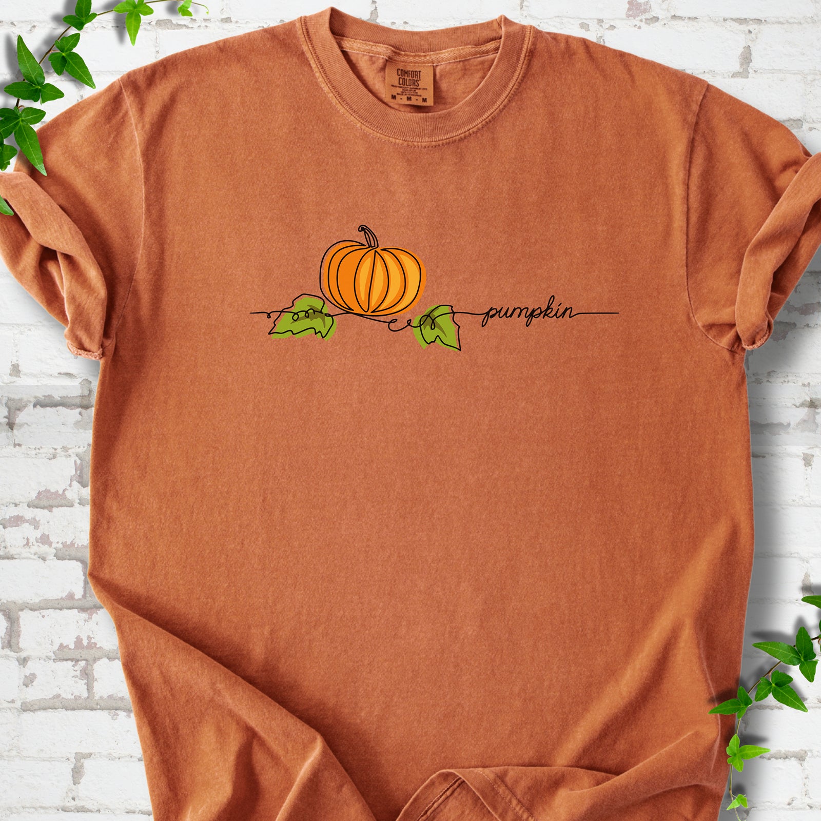 Yam Comfort Colors® T-shirt flat lay featuring a minimalist orange pumpkin, green leaves and delicate black script.