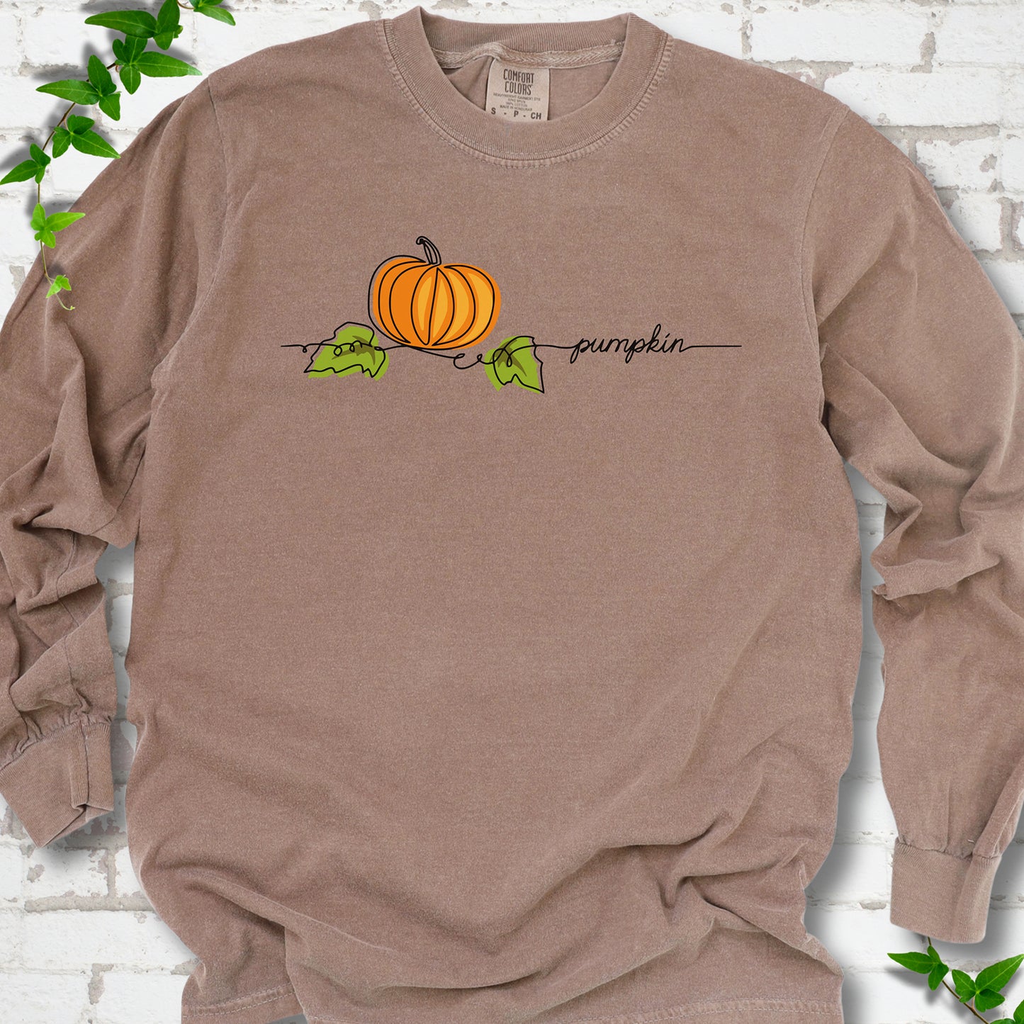 Espresso Comfort Colors® long sleeve T-shirt flat lay featuring a minimalist orange pumpkin, green leaves and delicate black script.