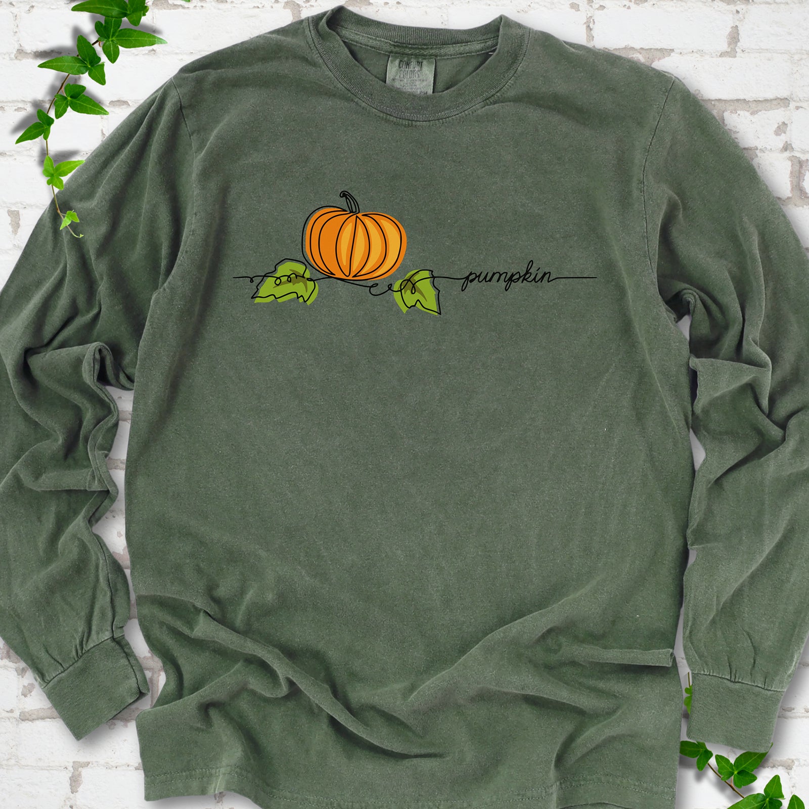 Hemp Comfort Colors® long sleeve T-shirt flat lay featuring a minimalist orange pumpkin, green leaves and delicate black script.