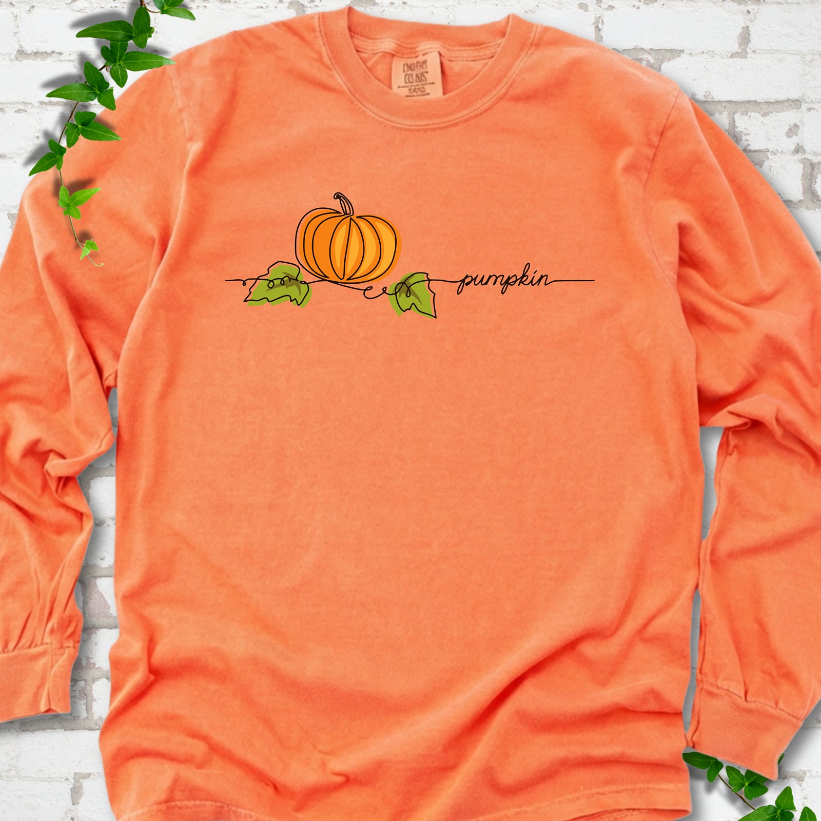 Melon Comfort Colors® long sleeve T-shirt flat lay featuring a minimalist orange pumpkin, green leaves and delicate black script.