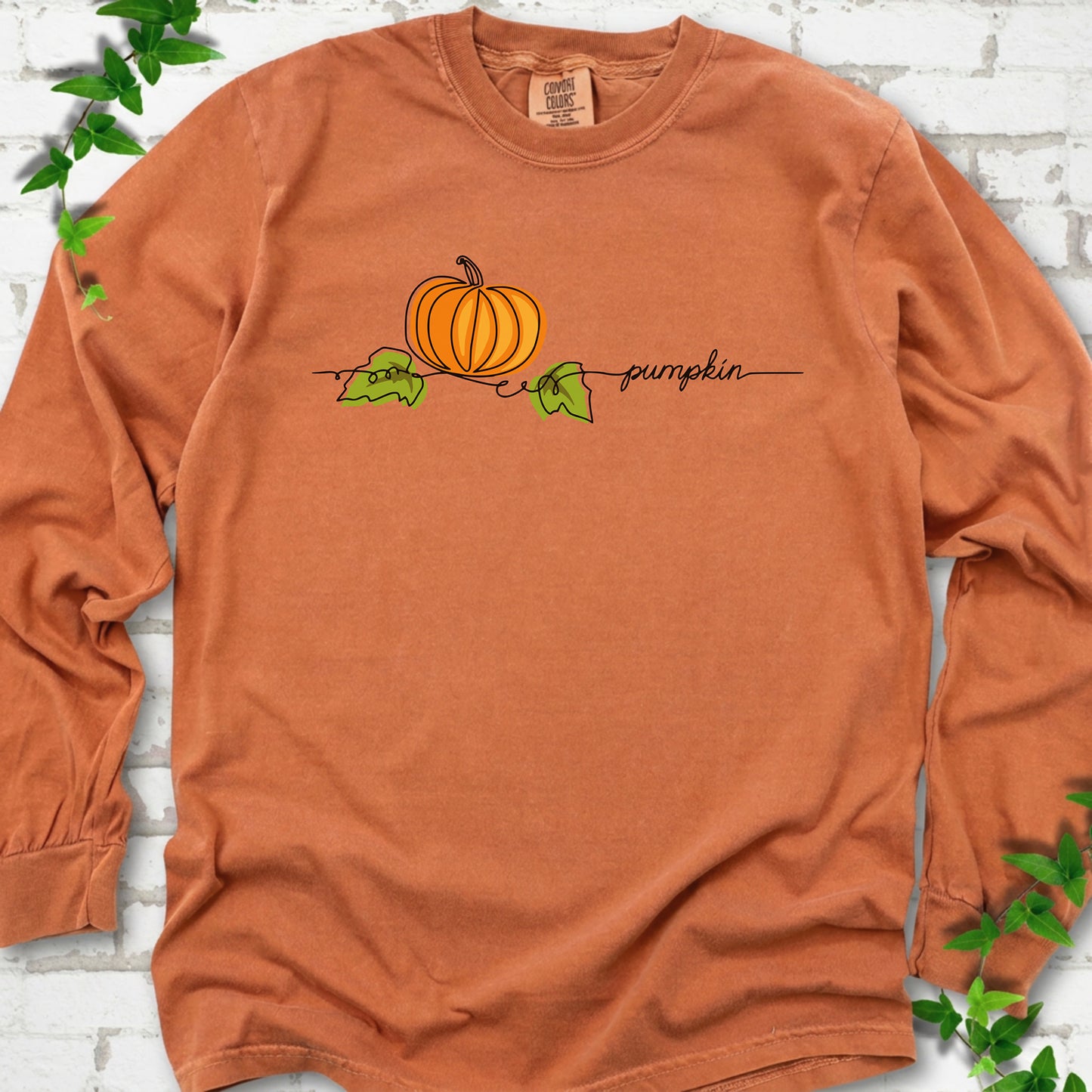 Yam Comfort Colors® long sleeve T-shirt flat lay featuring a minimalist orange pumpkin, green leaves and delicate black script.