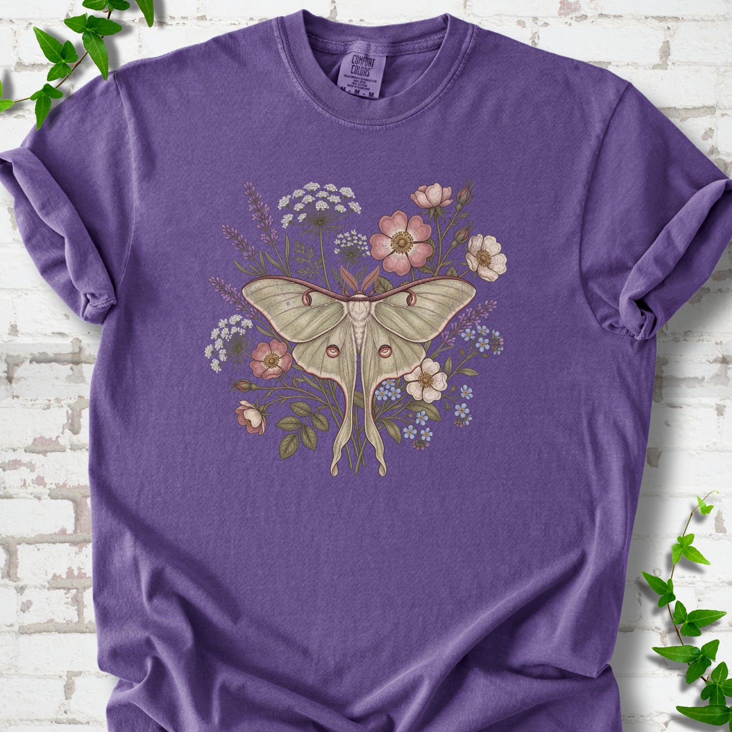 Grape Comfort Colors® T-shirt flat lay featuring a pale luna moth surrounded by pink, lavender, blue and white wildflowers.