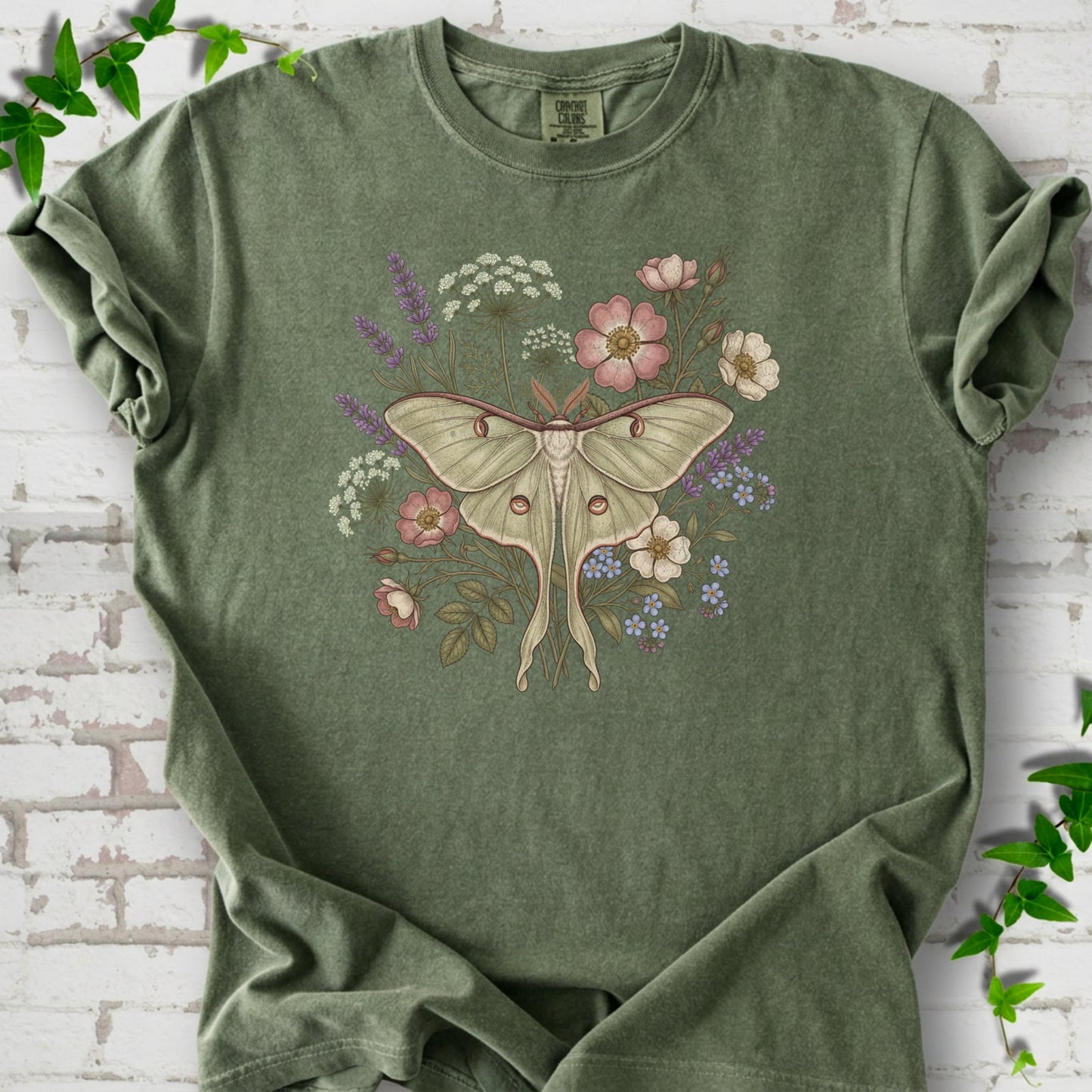 Moss Comfort Colors® T-shirt flat lay featuring a pale luna moth surrounded by pink, lavender, blue and white wildflowers.