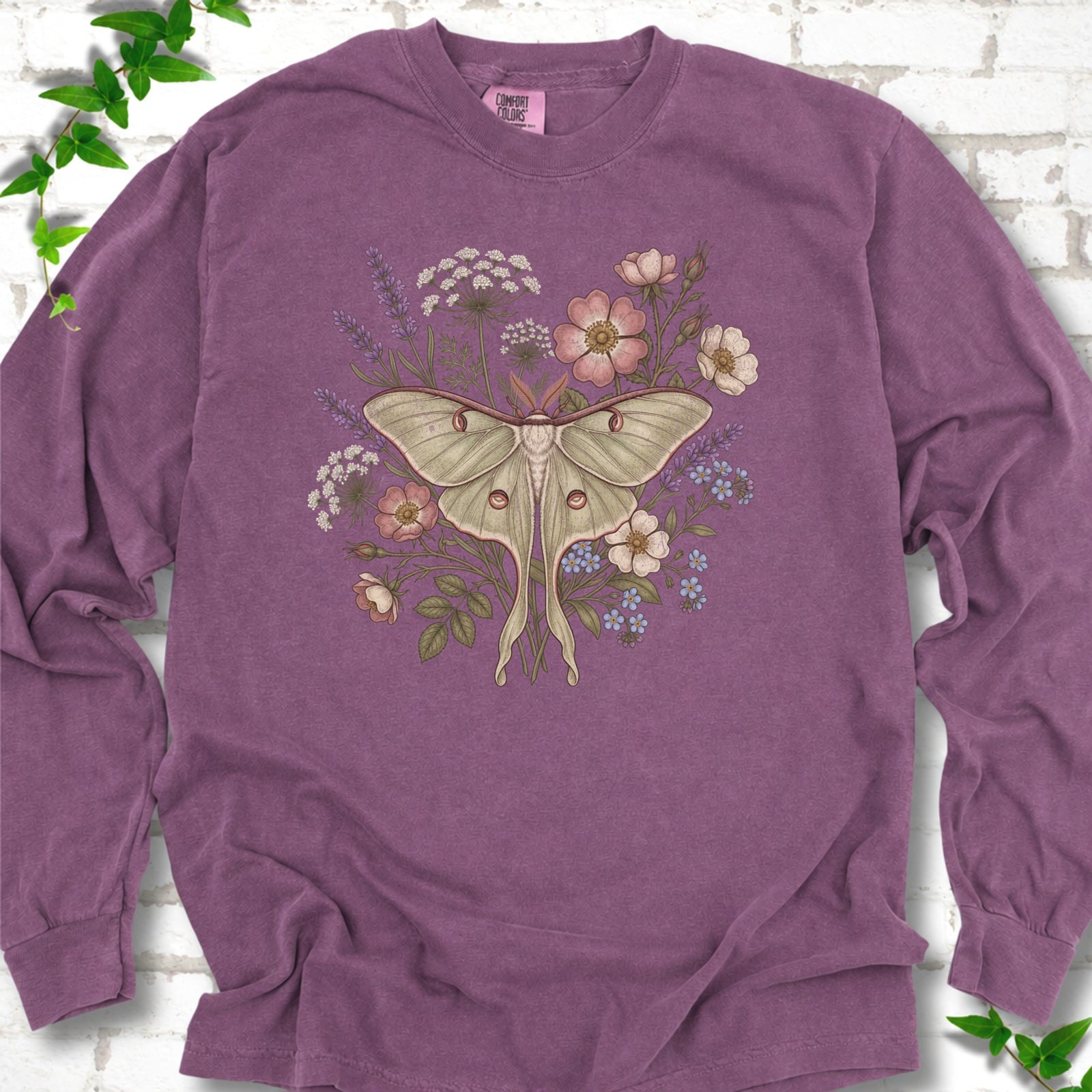 Berry Comfort Colors® long sleeve T-shirt flat lay featuring a pale luna moth surrounded by pink, lavender, blue and white wildflowers.