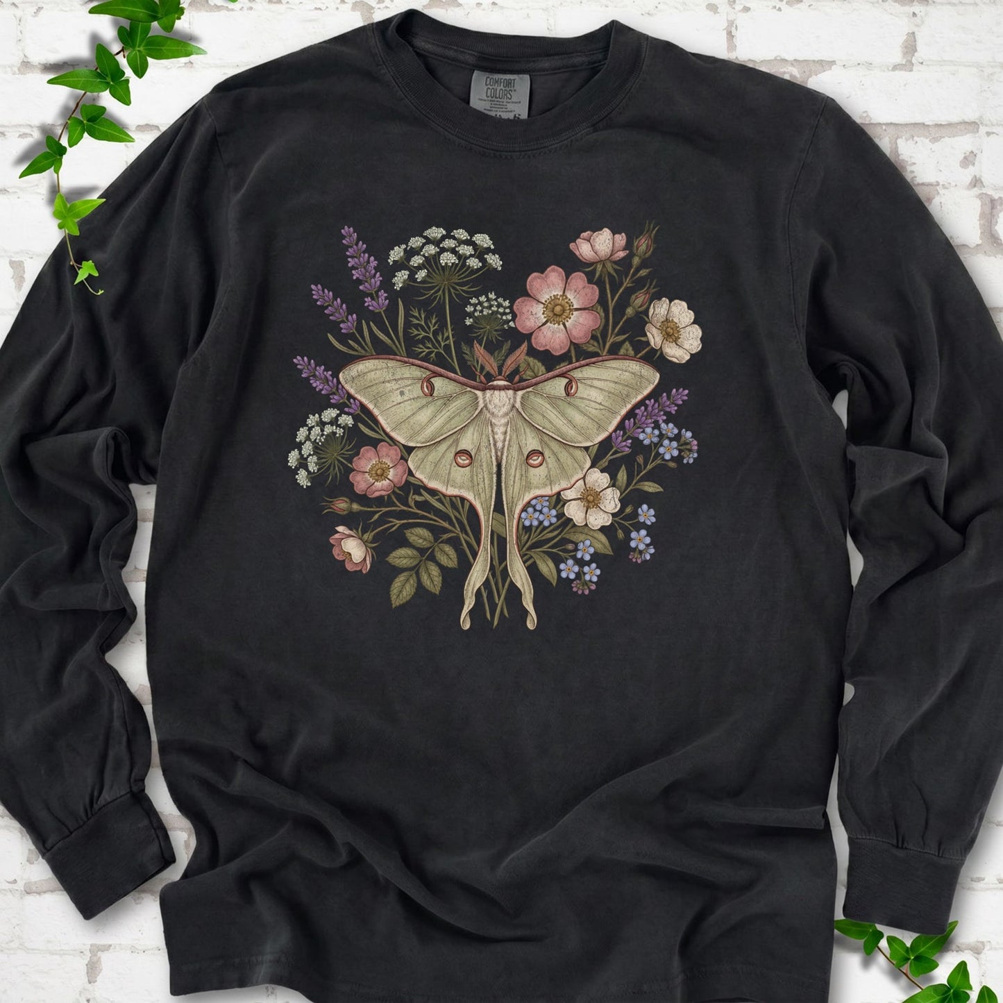 Black Comfort Colors® long sleeve T-shirt flat lay featuring a pale luna moth surrounded by pink, lavender, blue and white wildflowers.