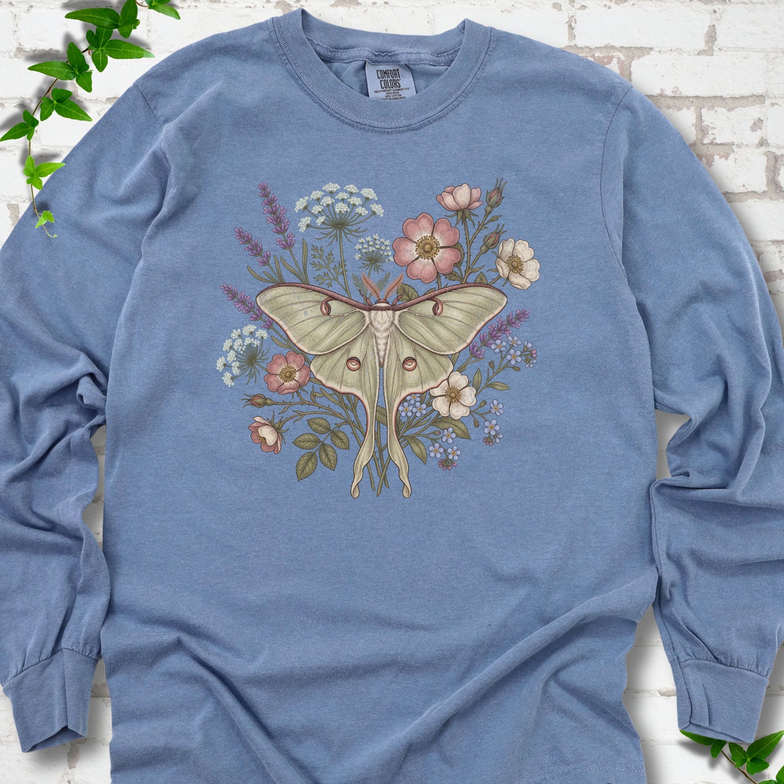 Blue Jean Comfort Colors® long sleeve T-shirt flat lay featuring a pale luna moth surrounded by pink, lavender, blue and white wildflowers.