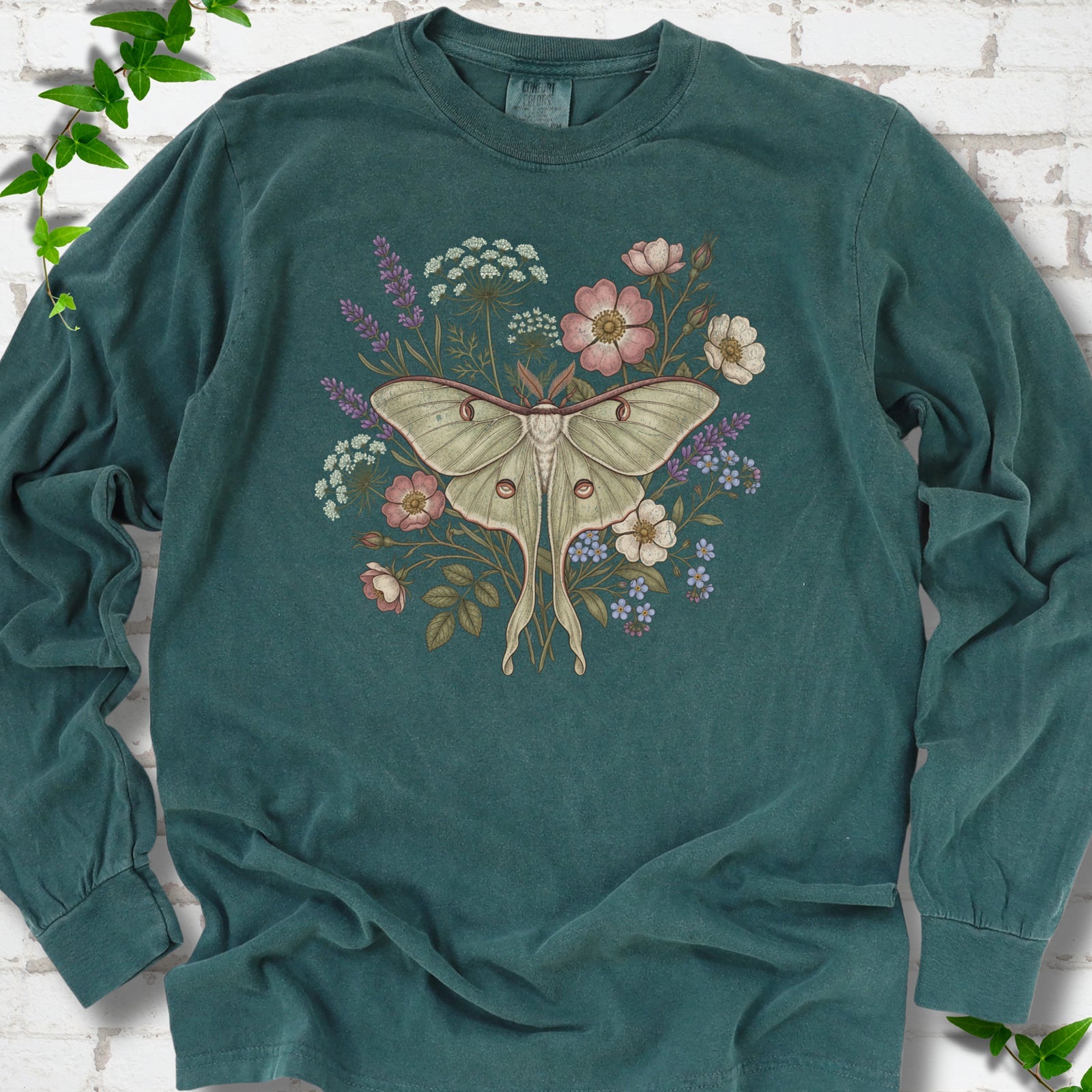 Blue Spruce Comfort Colors® long sleeve T-shirt flat lay featuring a pale luna moth surrounded by pink, lavender, blue and white wildflowers.