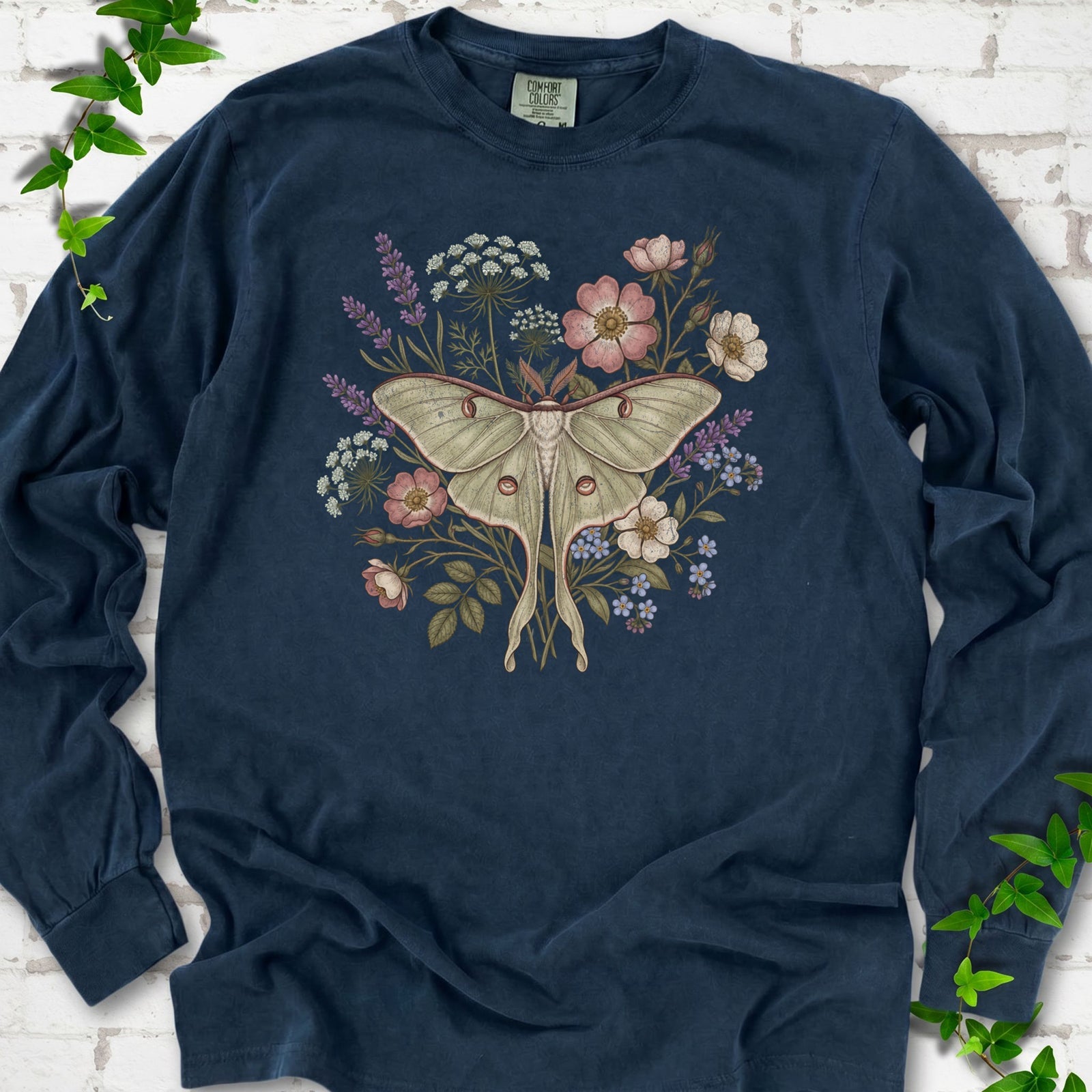 Midnight Comfort Colors® long sleeve T-shirt flat lay featuring a pale luna moth surrounded by pink, lavender, blue and white wildflowers.